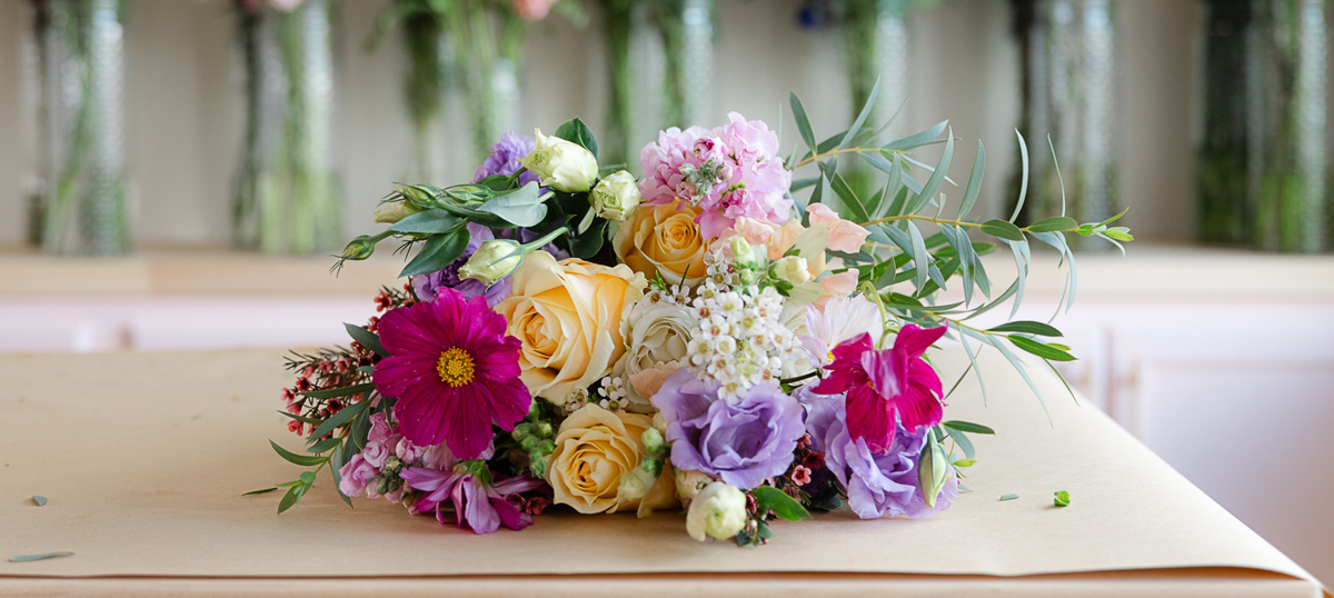 A vibrant mixed floral bouquet featuring yellow roses, magenta cosmos, purple lisianthus, and green foliage,
