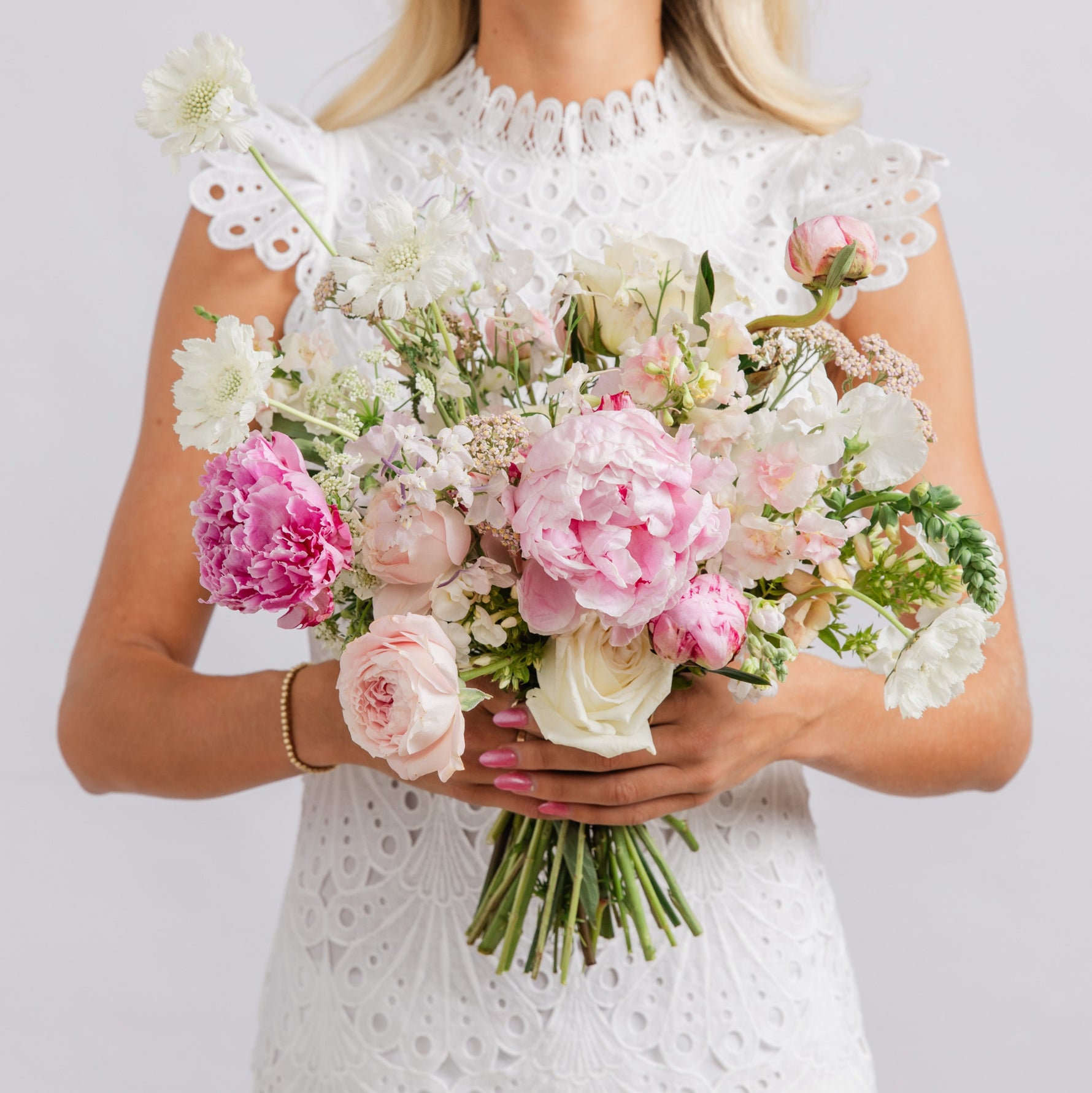 A bride holding a large bridal bouquet of pink and white flowers, including peonies, roses, and white chrysanthemums.