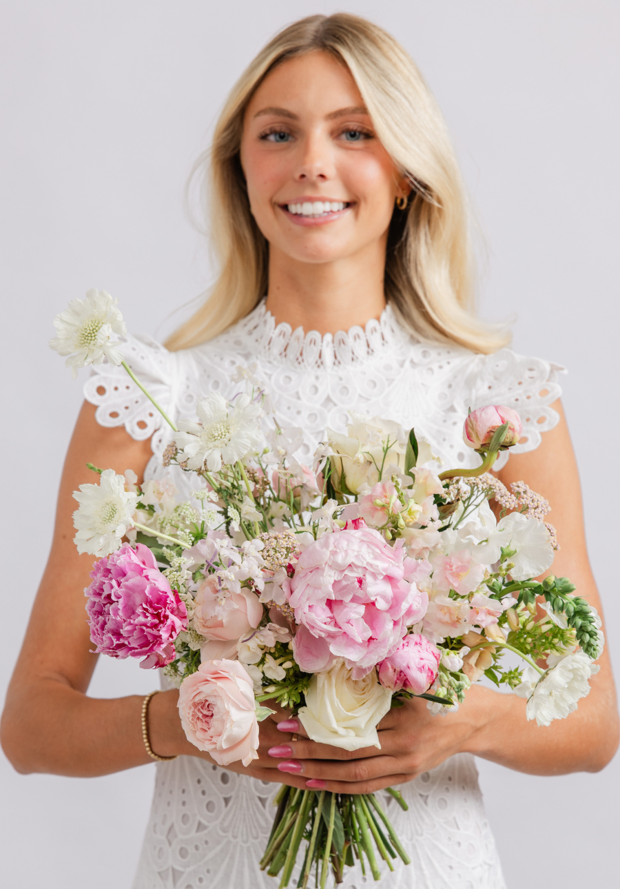 A smiling Utah bride in a white lace wedding dress holds a large, vibrant bouquet of pink, white, and light green flowers