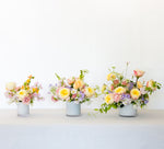 Three-tiered floral arrangements in milky white vases with fresh, colorful blooms and greenery.