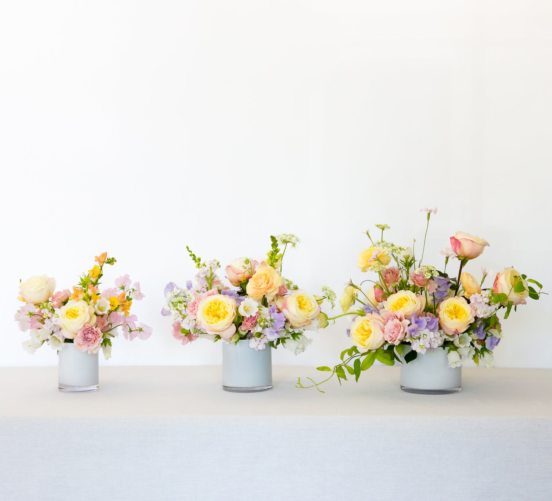 Three-tiered floral arrangements in milky white vases with fresh, colorful blooms and greenery.