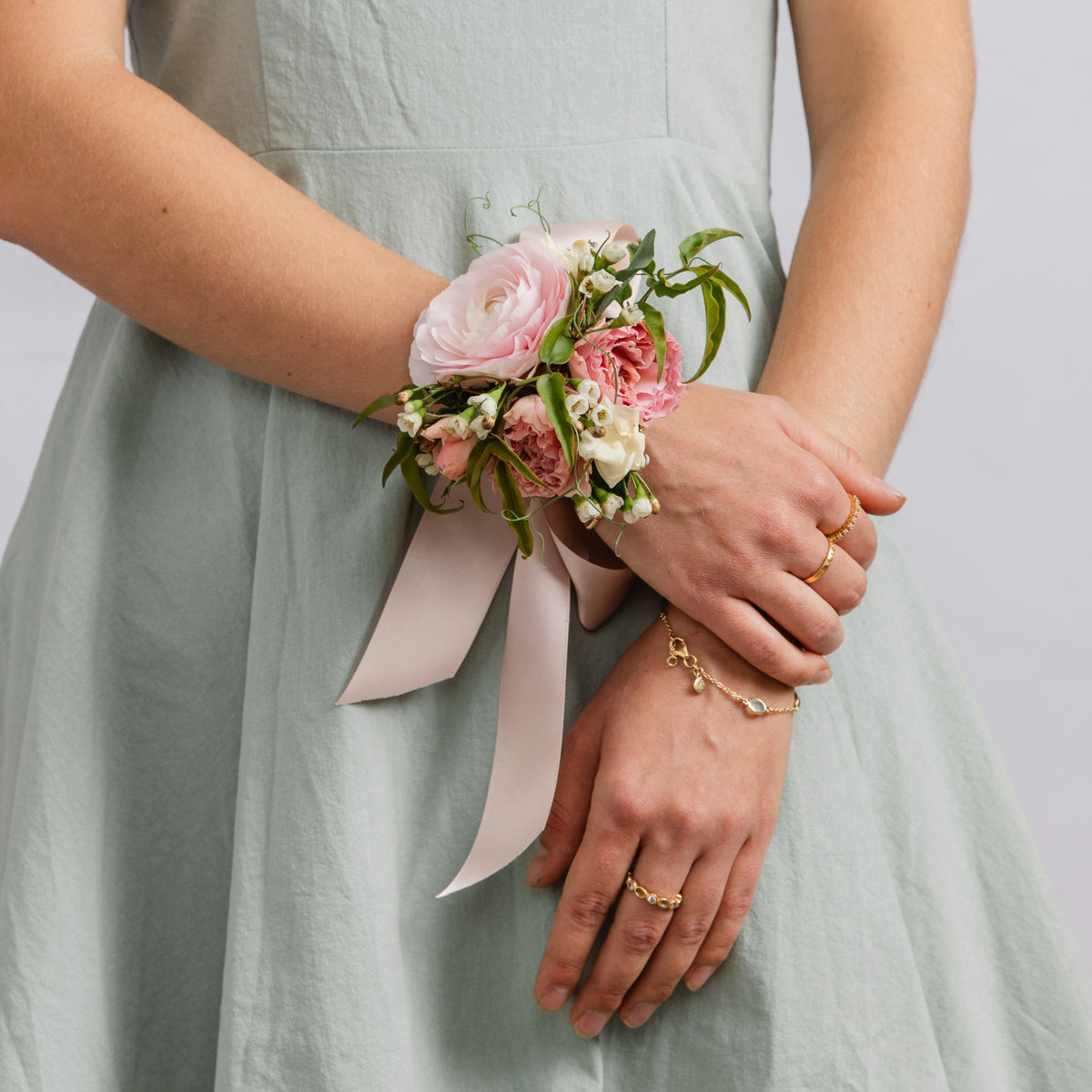 A woman wearing a floral wrist dance or wedding corsage with pink and white flowers, green leaves, and a light pink ribbon.