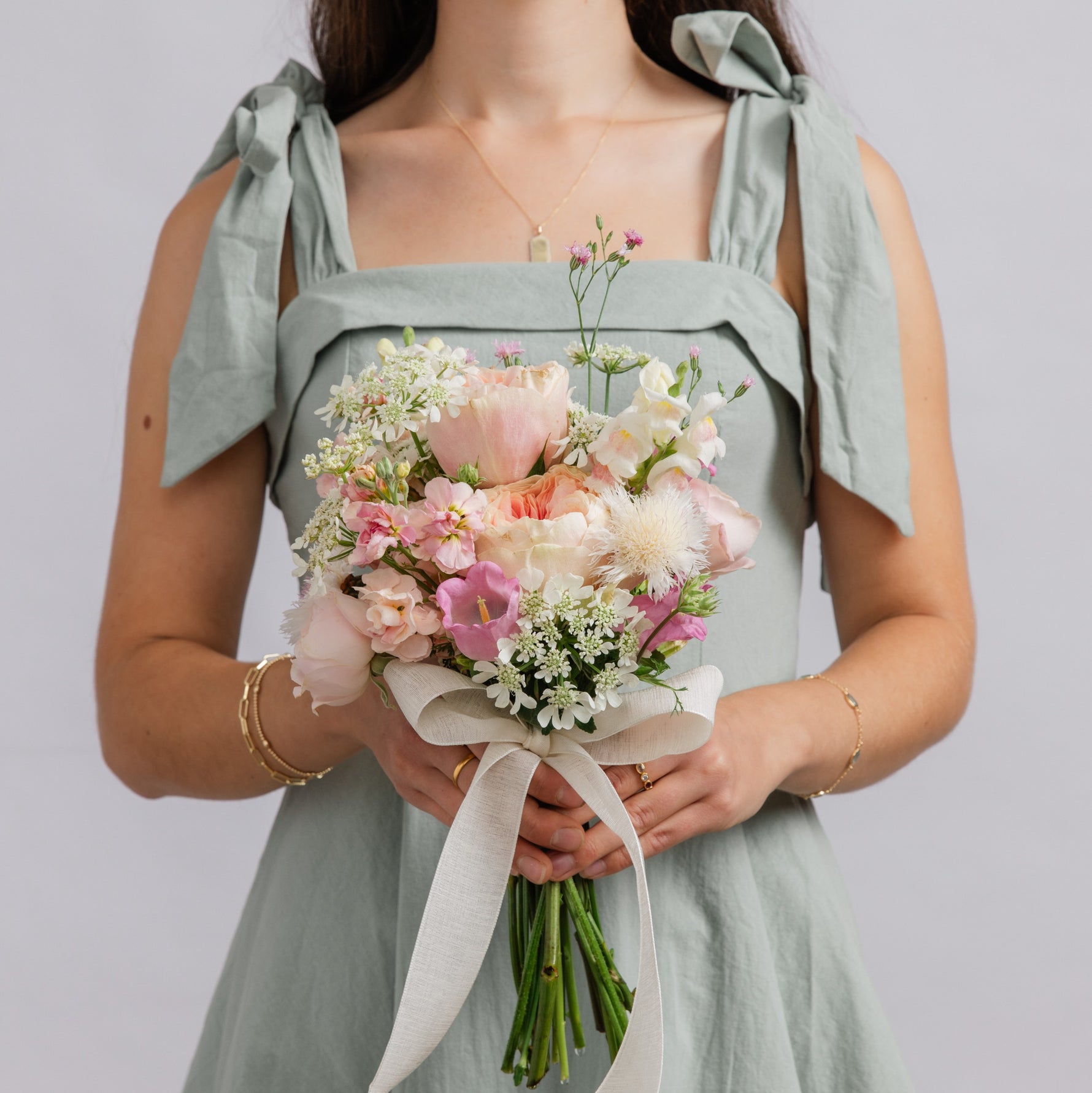 A woman holds a pastel pink and white flower dance posy bouquet with a cream ribbon
