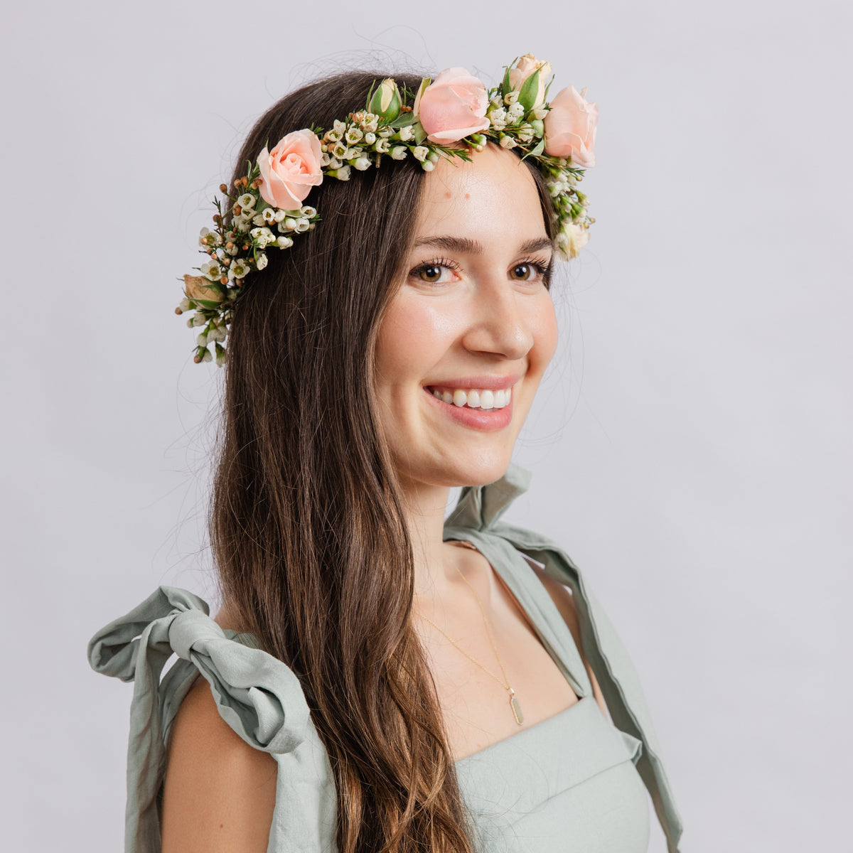 A woman wearing a floral crown of pink roses and green leaves, for weddings or dances.