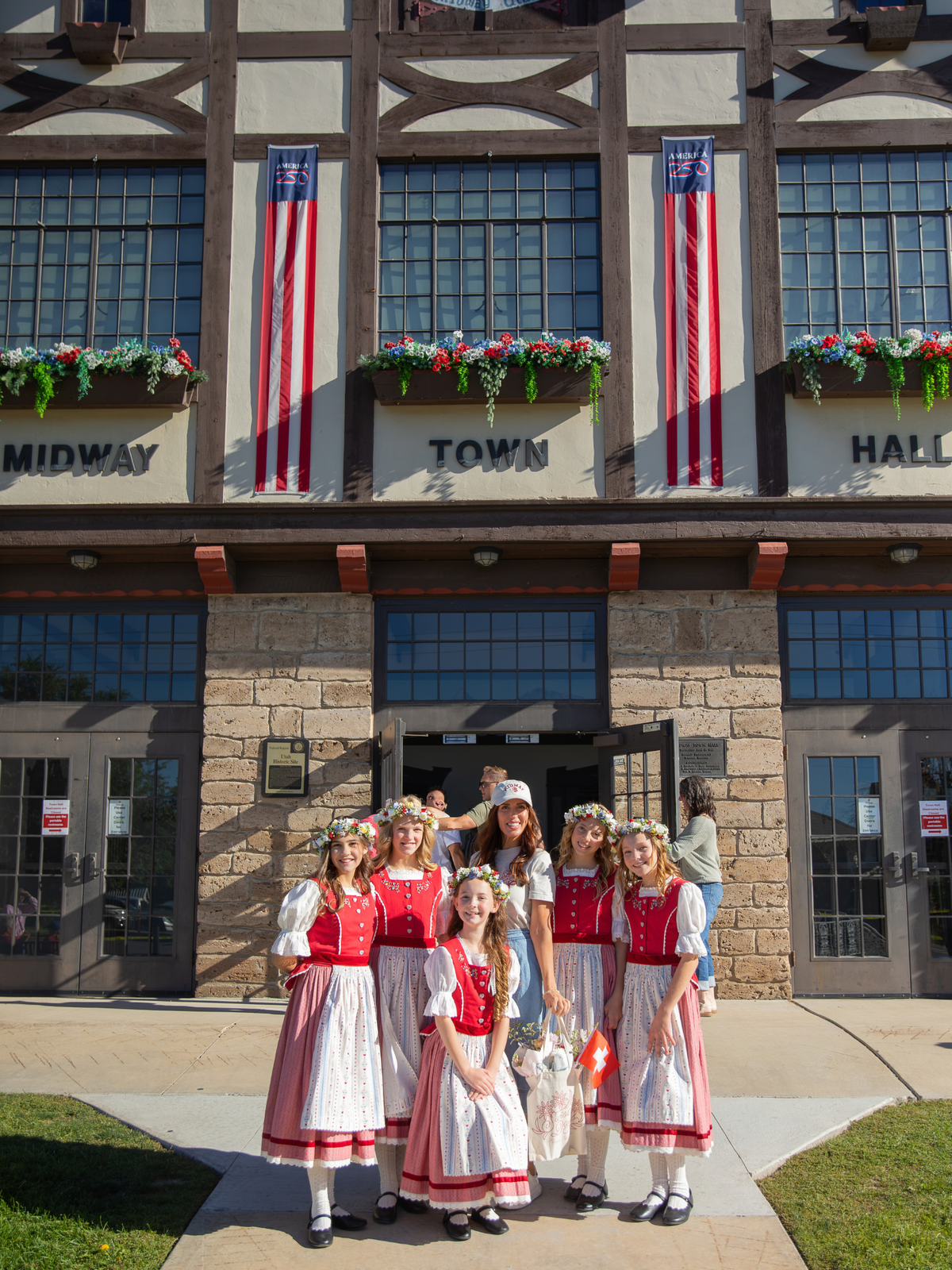Flower Bar Co. founder and florist Shawen Bailey poses with the Midway Swiss Miss group of young ladies in front of a historic Midway Town Hall building during Swiss Days.