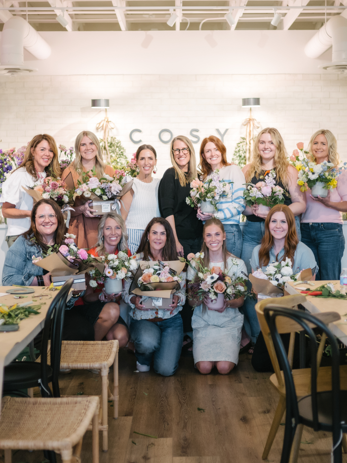 A group of women attends a flower workshop, each holding a small bouquet of florals