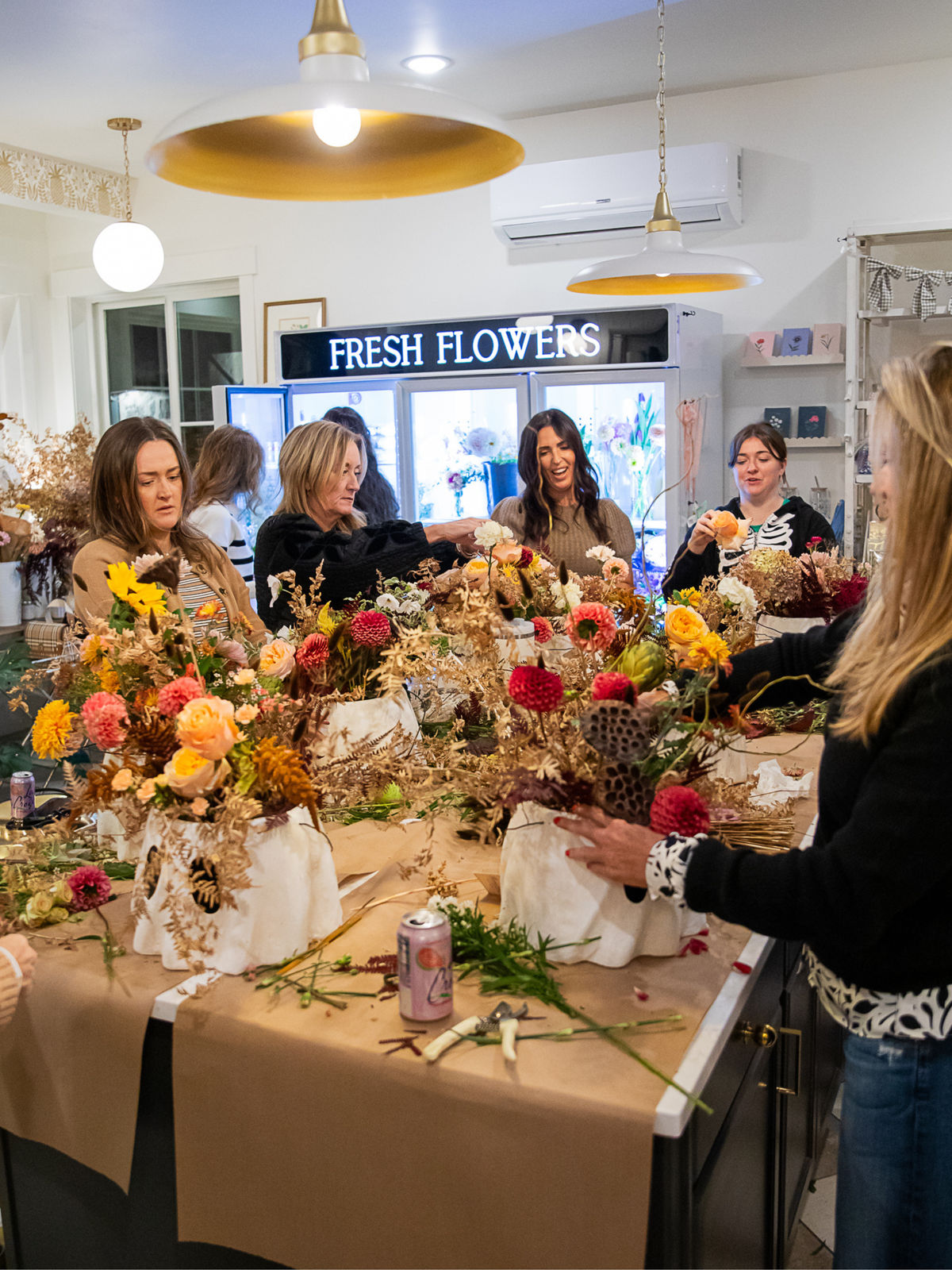 A group of women working together at a table filled with colorful fresh flowers and dried floral arrangements at a flower shop in Midway, Utah