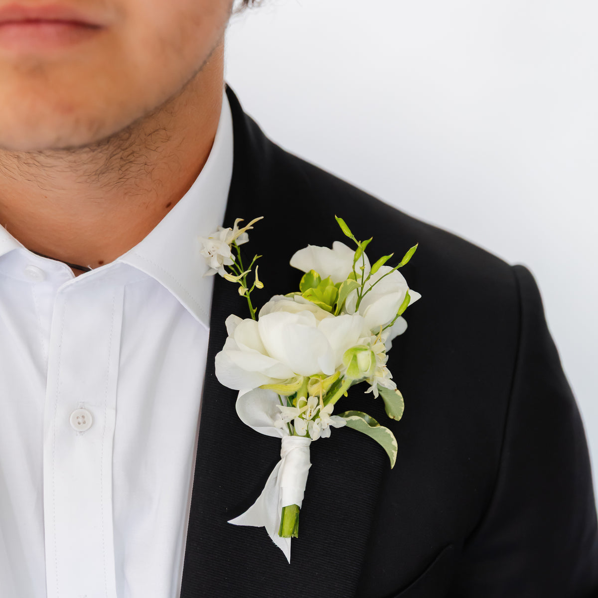 A black tuxedo jacket and white dress shirt, featuring a white floral wedding or dance boutonniere with green stems on his left lapel.