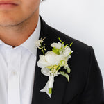 A black tuxedo jacket and white dress shirt, featuring a white floral wedding or dance boutonniere with green stems on his left lapel.