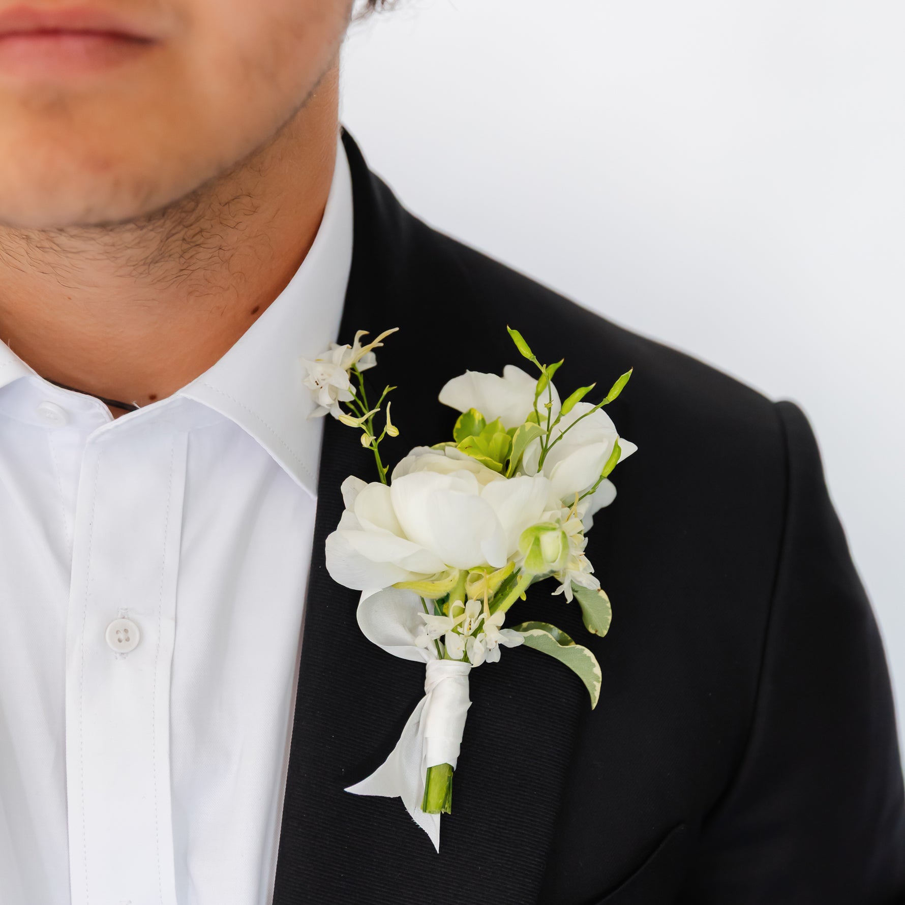 A black tuxedo jacket and white dress shirt, featuring a white floral wedding or dance boutonniere with green stems on his left lapel.