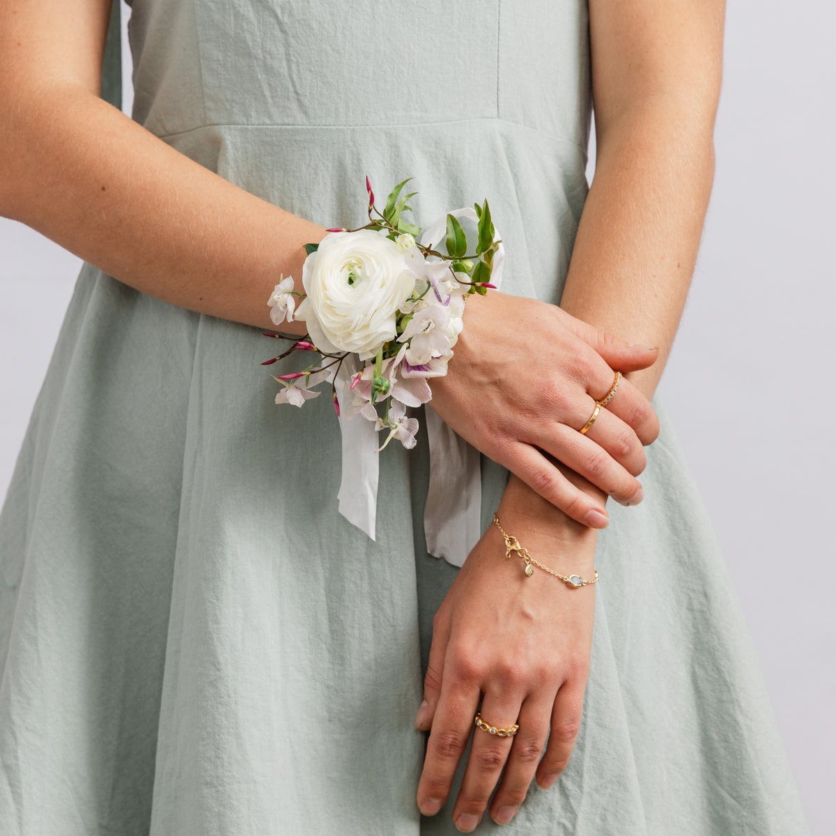A woman wearing a white floral wrist corsage with green leaves and white ribbons, for weddings or school dances.