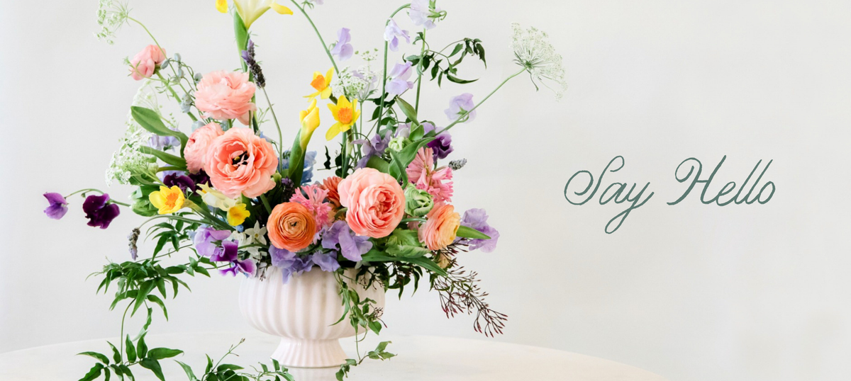 A pastel pink, purple, and yellow garden floral arrangement in a white ribbed vase 