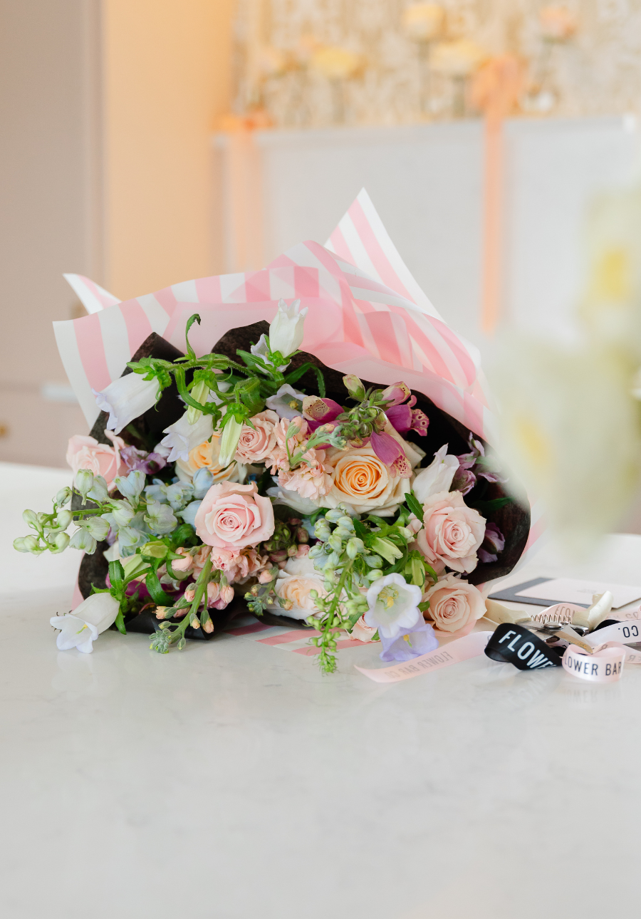 A wrapped bouquet of pastel pink, peach, purple, and white flowers from Flower Bar Co. local Utah florist flower delivery subscriptions