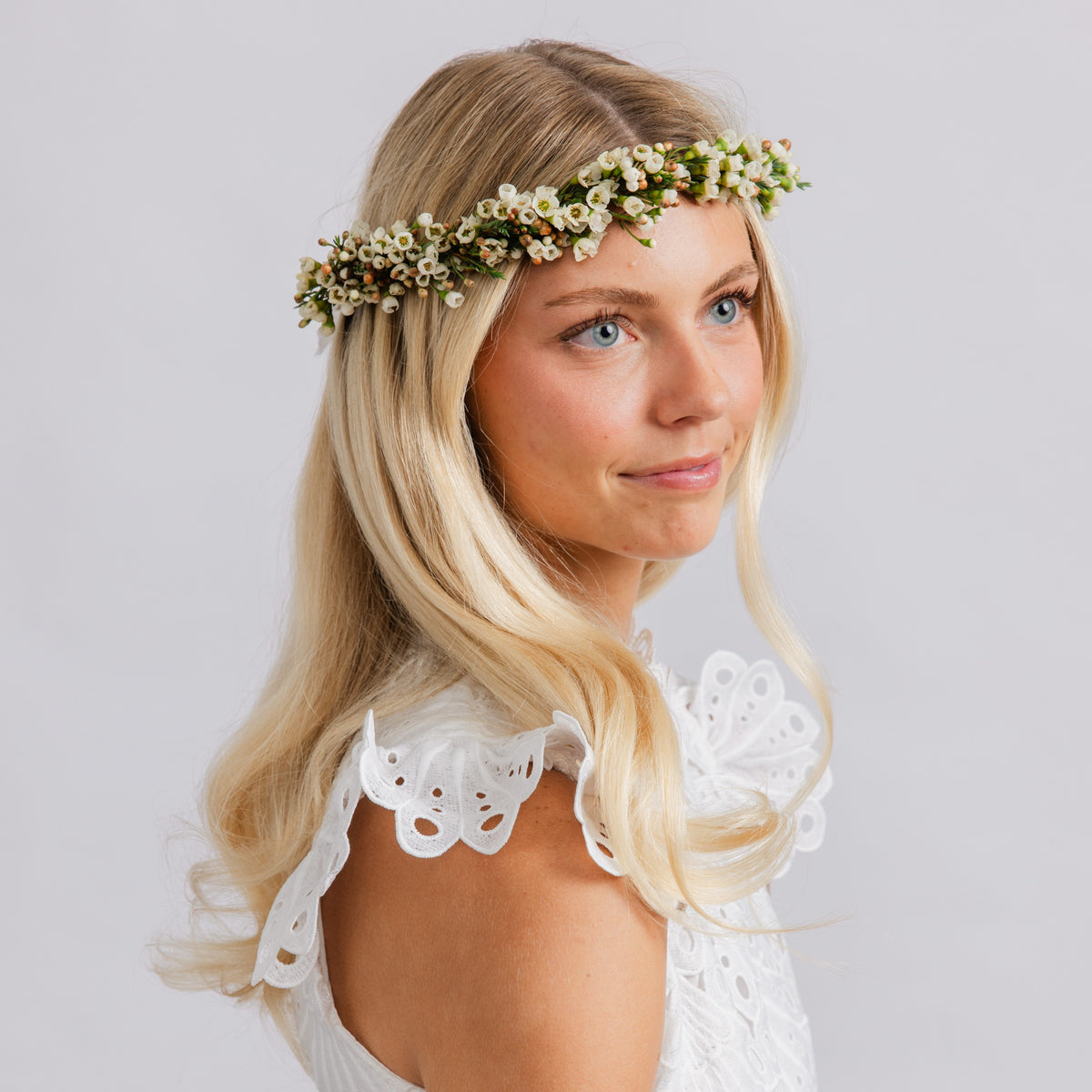 A woman wearing a delicate white floral crown with small white blossoms and green leaves, for weddings or dances.