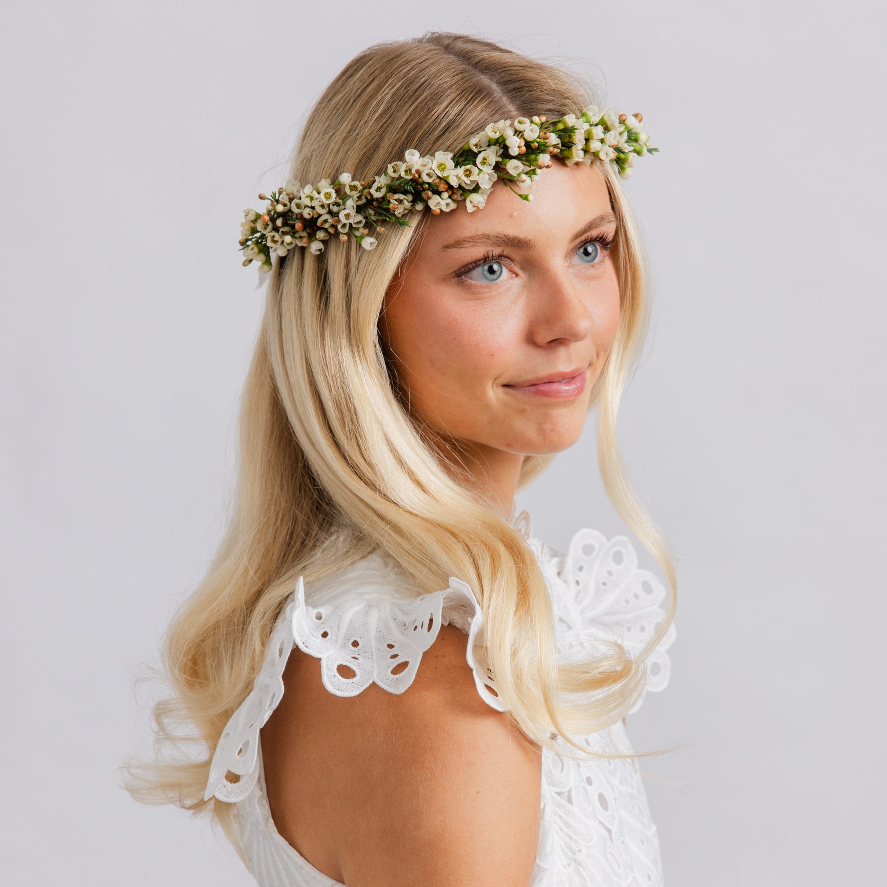 A woman wearing a delicate white floral crown with small white blossoms and green leaves, for weddings or dances.
