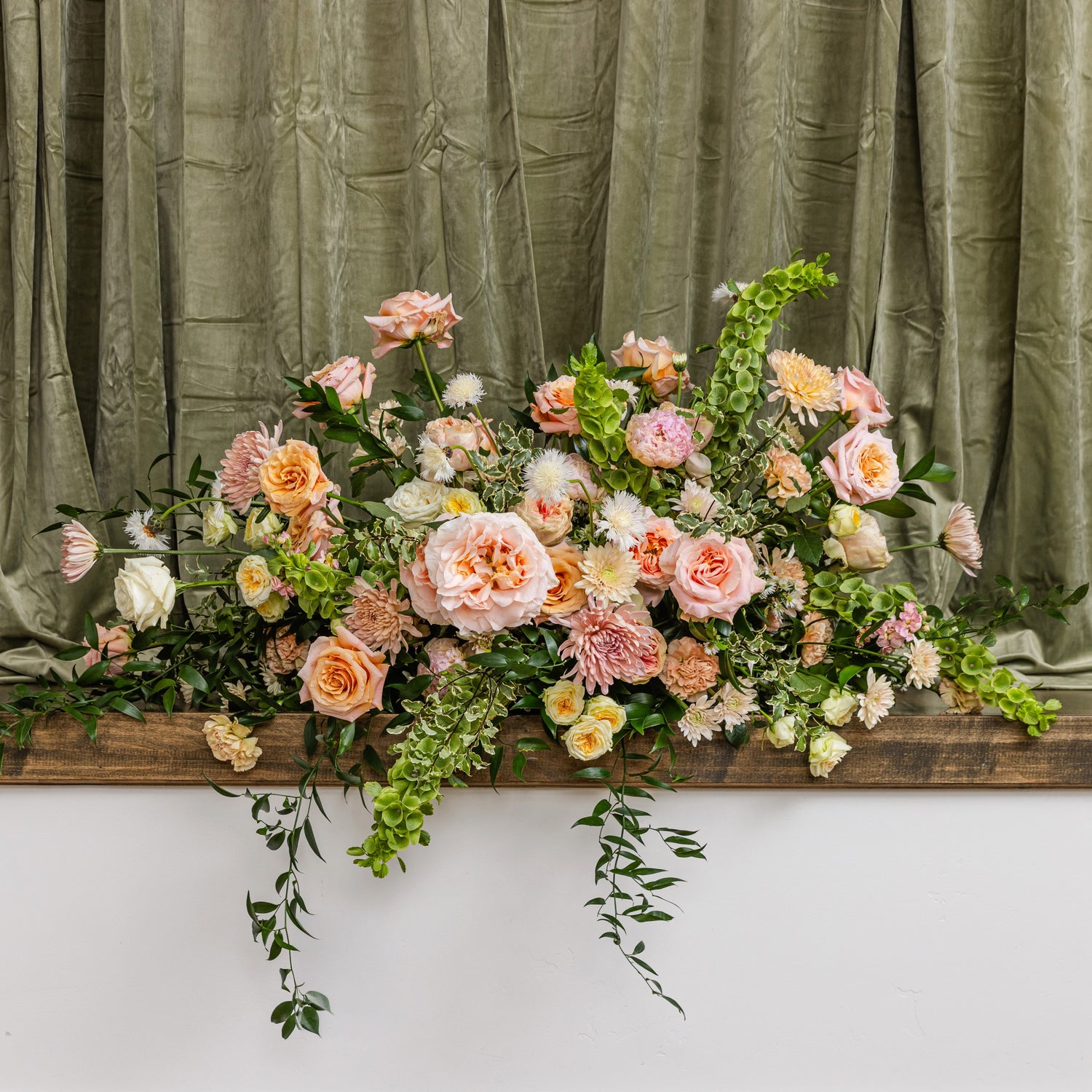 A large floral casket arrangement in soft peach, pink, cream, and green foliage.