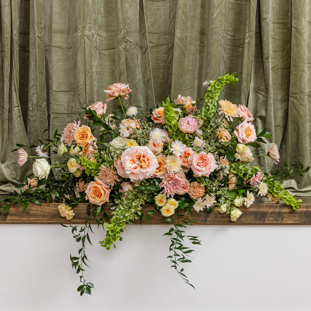 A large floral casket arrangement in soft peach, pink, cream, and green foliage.