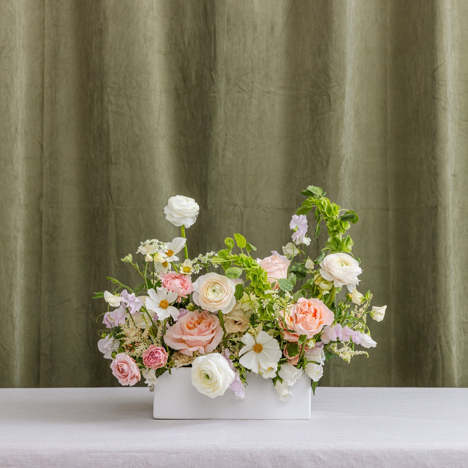 A floral arrangement of pink, white, and light purple flowers in a white rectangular planter.
