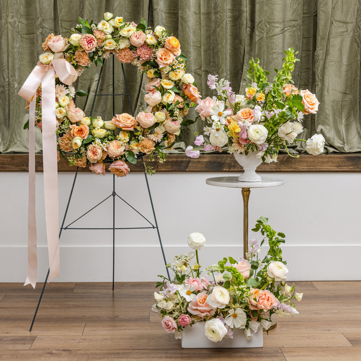A sympathy floral arrangement display featuring a large arch and multiple bouquets in soft peach, pink, cream, and white tones.