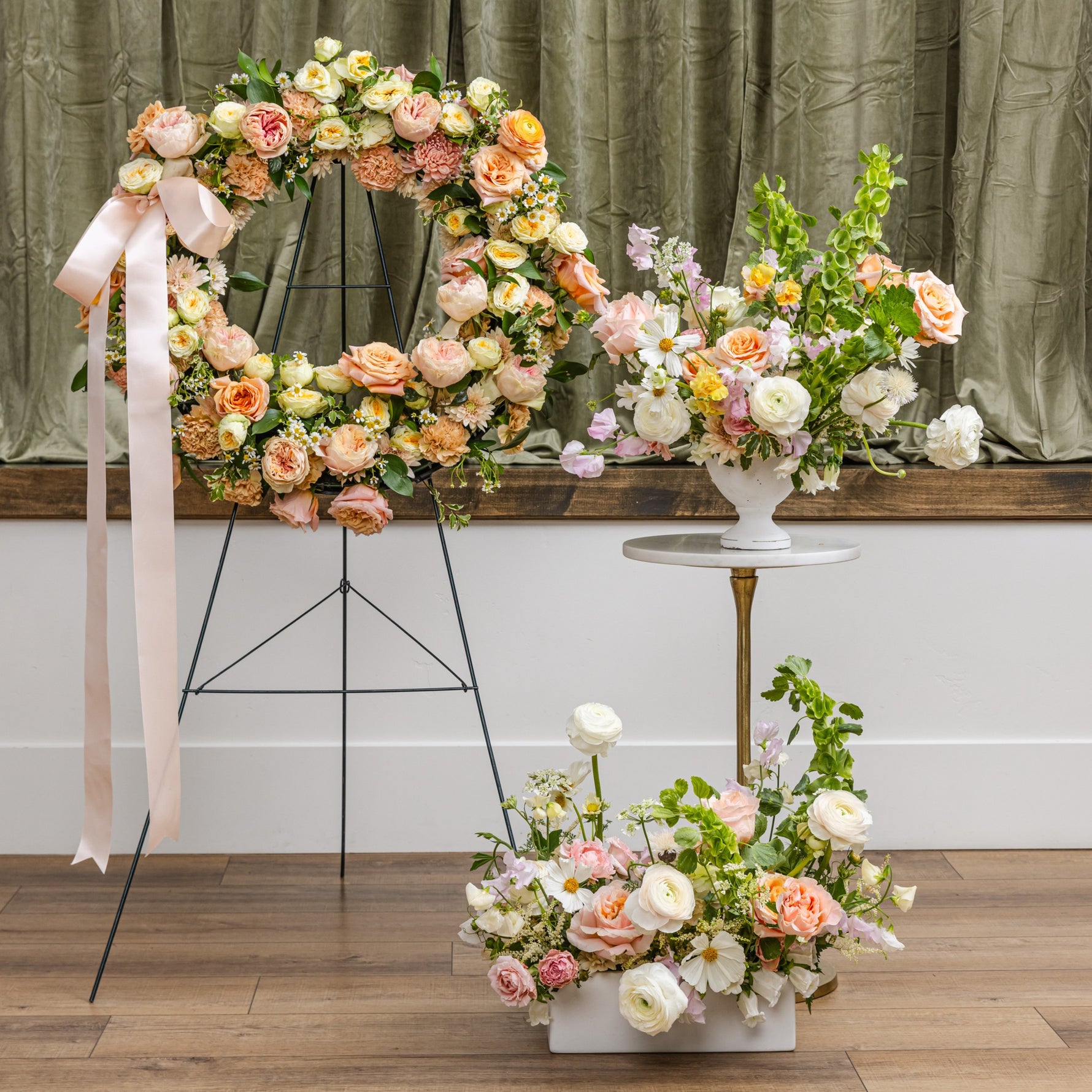 A sympathy floral arrangement display featuring a large arch and multiple bouquets in soft peach, pink, cream, and white tones.