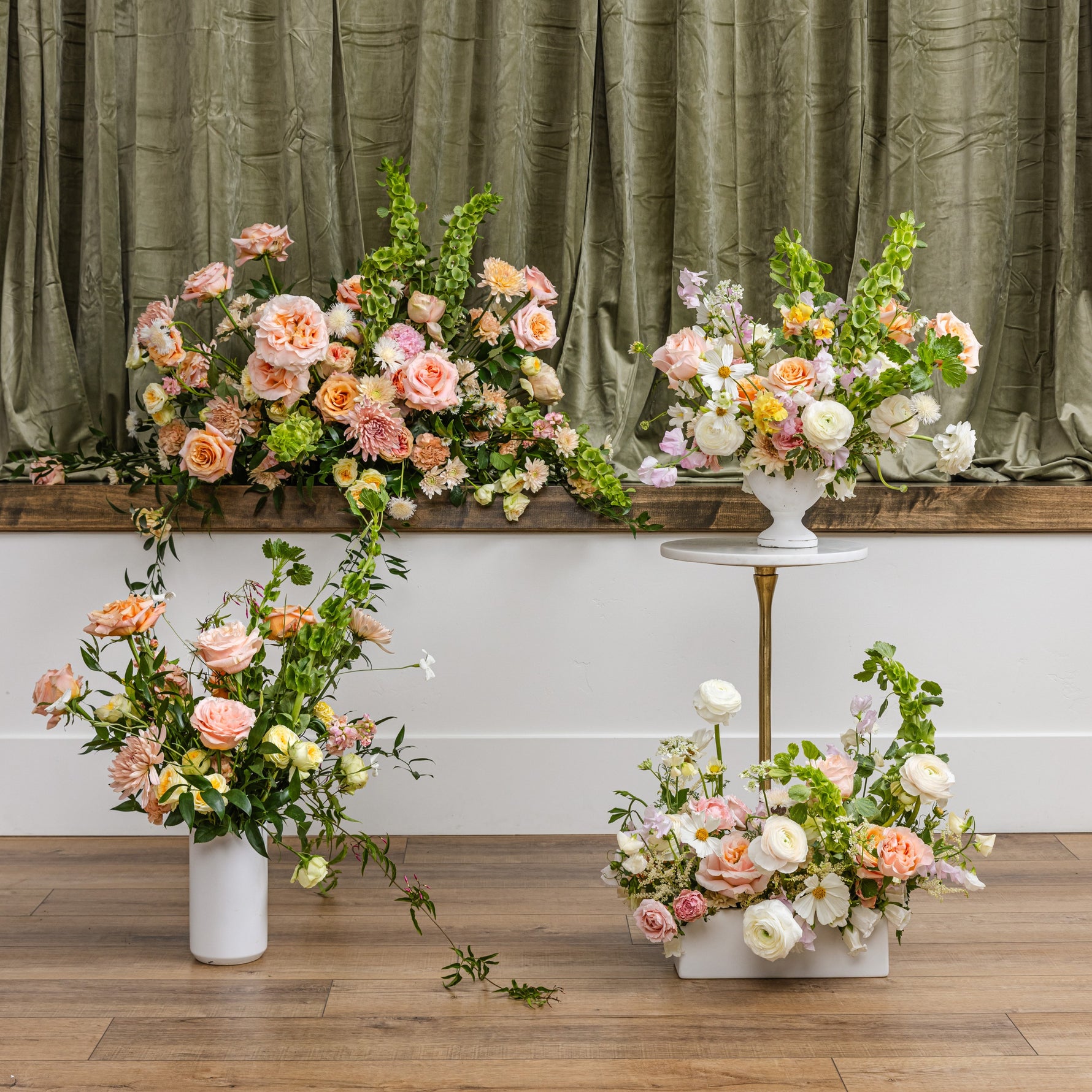 Four sympathy floral arrangement display featuring a large arch and multiple bouquets in soft peach, pink, cream, and white tones.