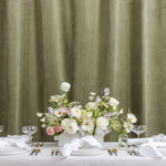 A styled wedding table set with white plates, folded napkins, silver cutlery, and wine glasses. A white vase filled with a pastel floral arrangement sits in the center.
