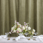 A styled wedding table setup with white tablecloths, folded napkins, silver cutlery, clear wine glasses, and a central floral arrangement in a white vase.