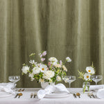A styled wedding table setup with white tablecloths, white plates, clear wine glasses, silver cutlery, and neutral floral centerpieces.