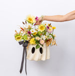 A ghost-shaped cream-colored planter filled with a colorful fall wildflower arrangement, including yellow daisies, white flowers, and green foliage.