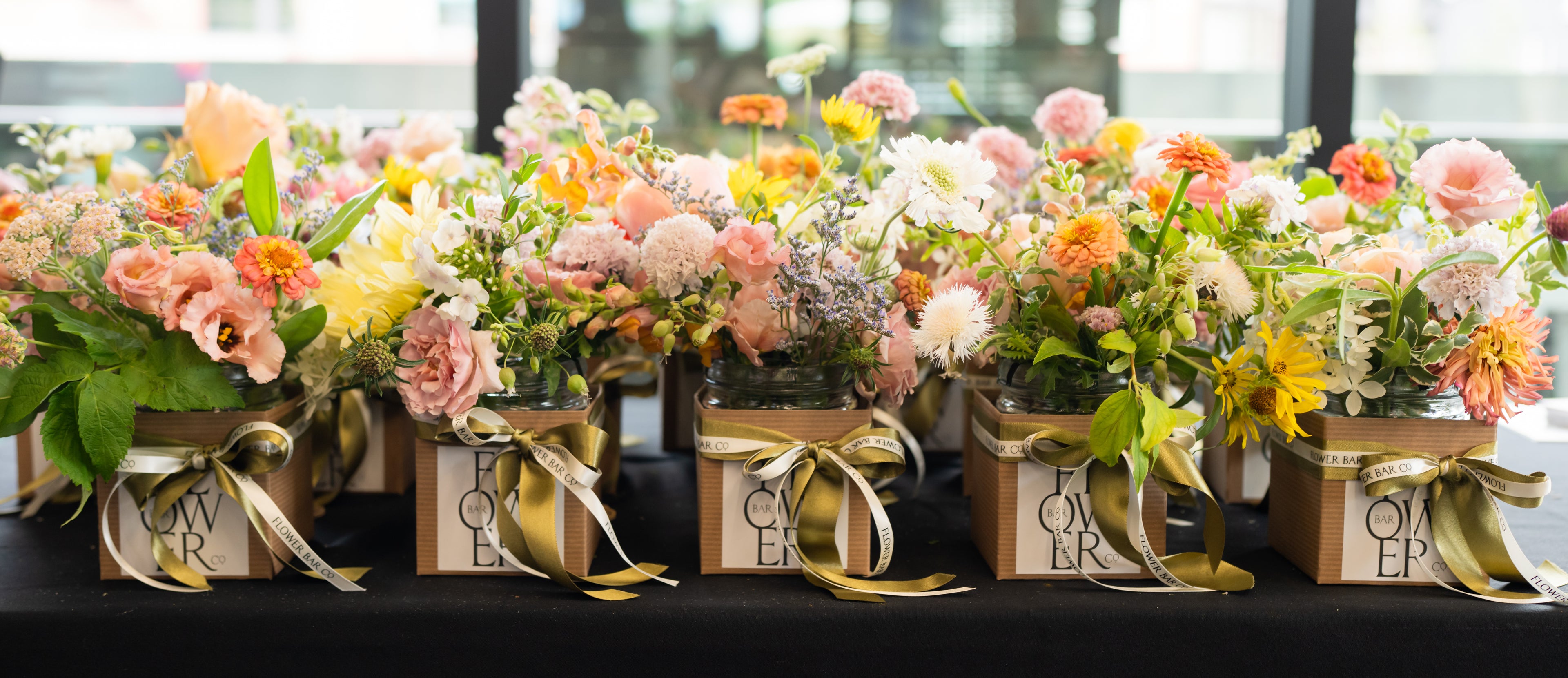 Flower Bar Co colorful floral arrangements in small kraft gift boxes tied with gold ribbons