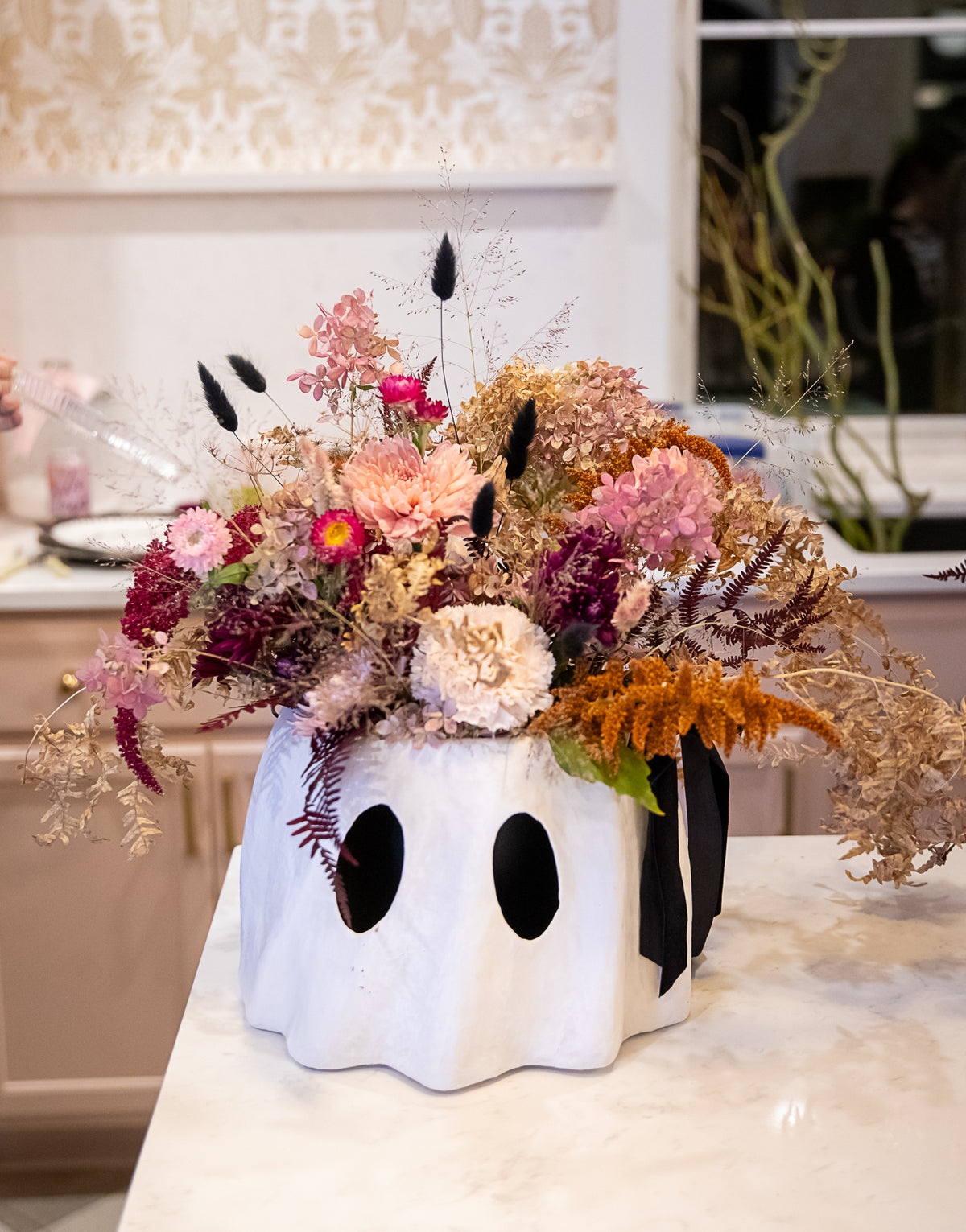 A white ghost-shaped bucket planter filled with a colorful dried flower arrangement in pink, beige, orange, and burgundy.